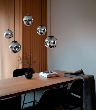 Elegantes Esszimmer mit Holztafel, schwarzen Stühlen und mehreren kugelförmigen Pendelleuchten aus glänzendem Metall über dem Tisch.