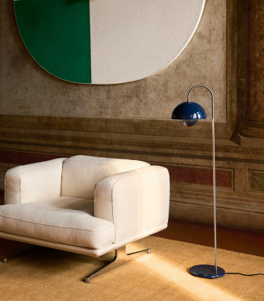 Elegante &Tradition Stehleuchte neben modernem Loungesessel in warmem Interieur.
