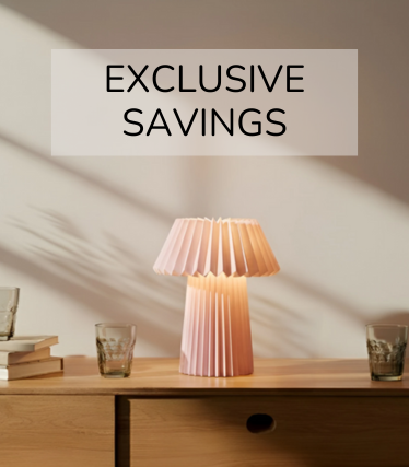 Zartrosa Tischleuchte auf einem Holzsideboard, umgeben von Gläsern und Büchern im warmen Sonnenlicht.