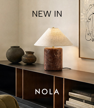 Tischleuchte von Nola mit rotbraunem Marmorfuß und konischem Leinenschirm auf einem dunklen Sideboard. Text: „New In – Nola“.
