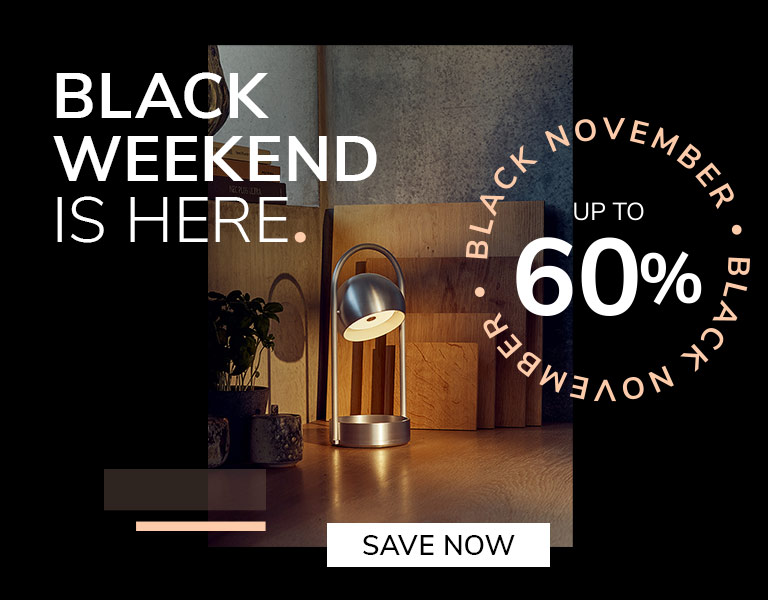 Save now Modern silver table lamp glowing on a wooden desk with cutting boards and plants in the background. Promotional text reads: ‘Black Weekend is here. Up to 60%. Black November.’ A button says ‘Save Now.’